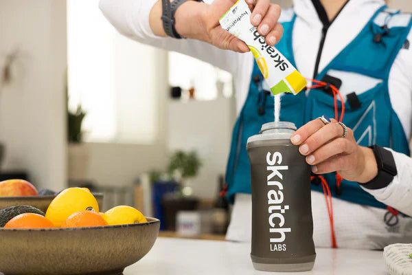 A cyclist is filling her water bottle with a Skratch Labs sport hydration mix in their kitchen.