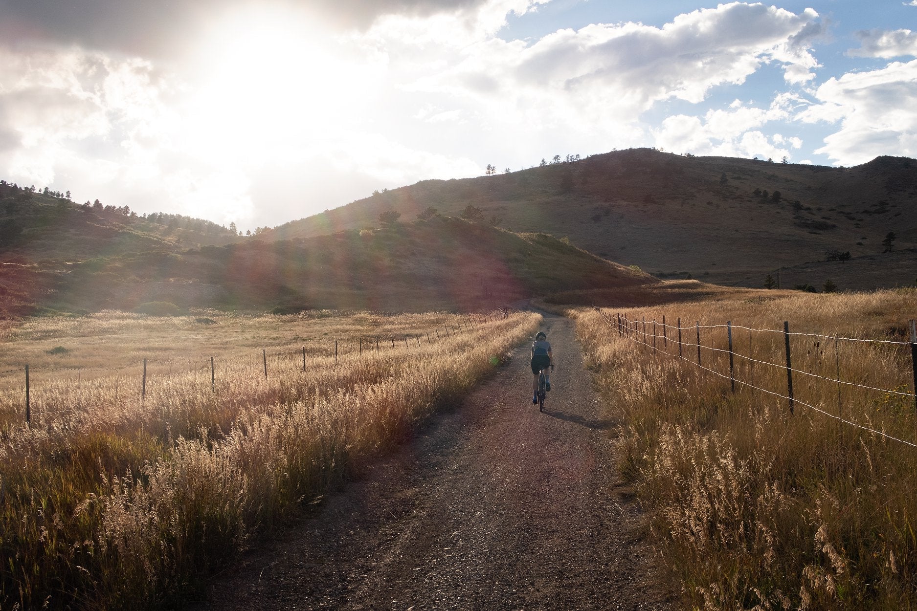 Someone riding a KindHuman Kensuke 2.0 carbon gravel bike down a dirt path in a wheat field.