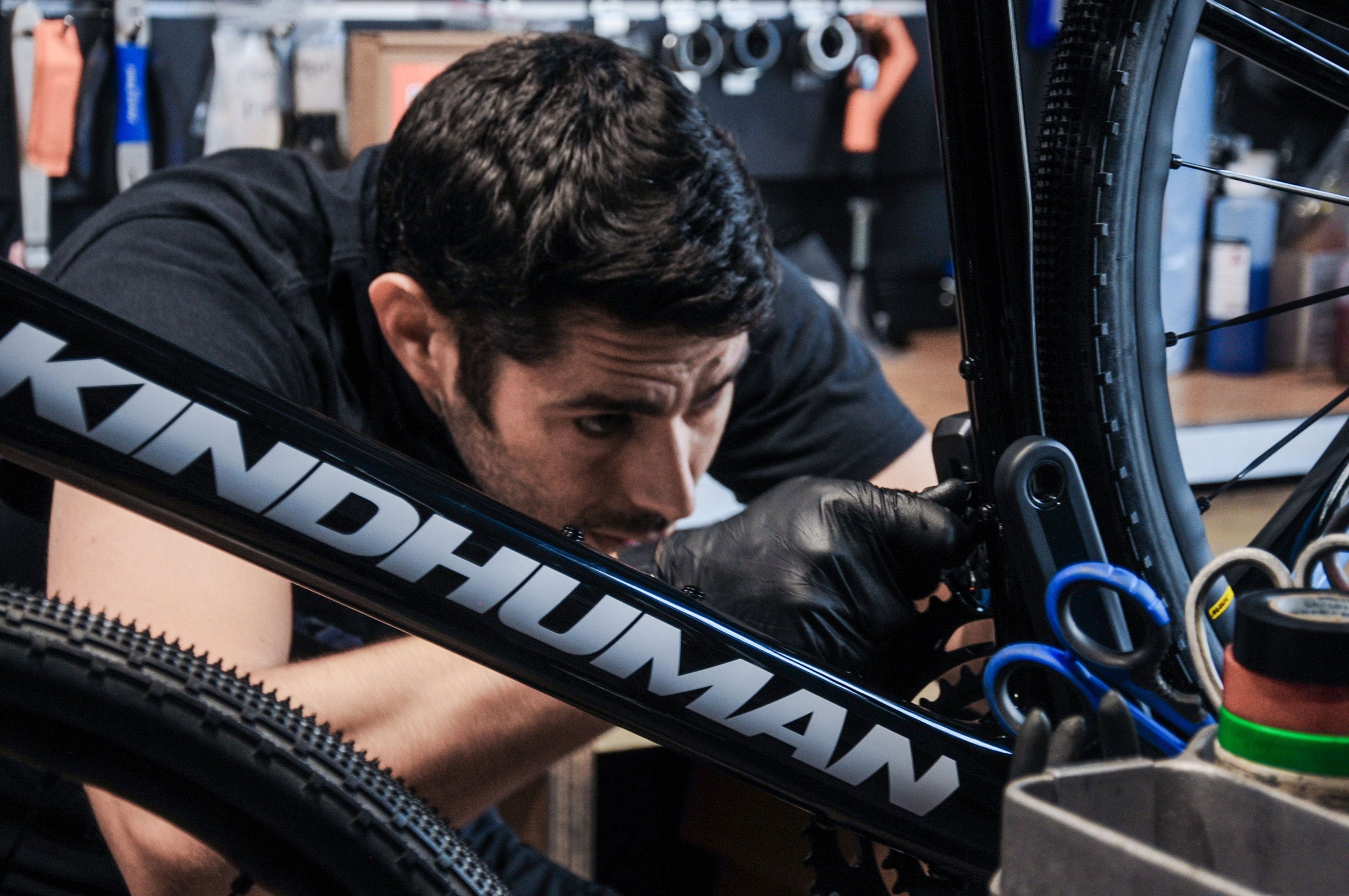 A bike mechanic is working on the front derailleur of a carbon gravel bike made by KindHuman Bicycles, the Kensuke 2.0.